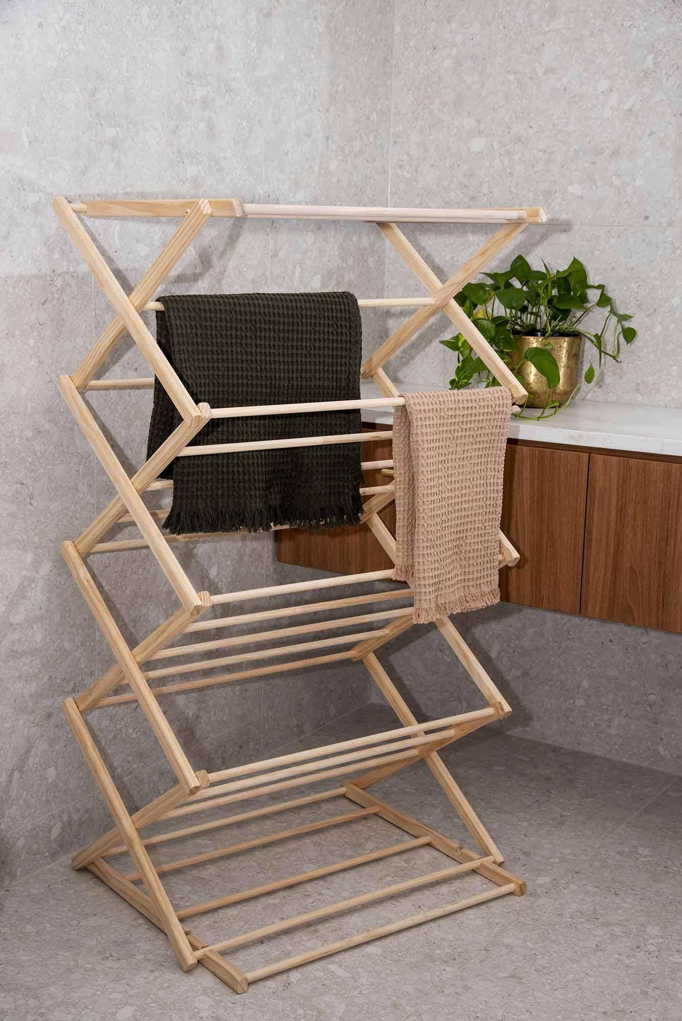 Wooden drying rack with clothes on a gray floor against a light gray wall. Victoria James Home Eco Deluxe Clothes Airer