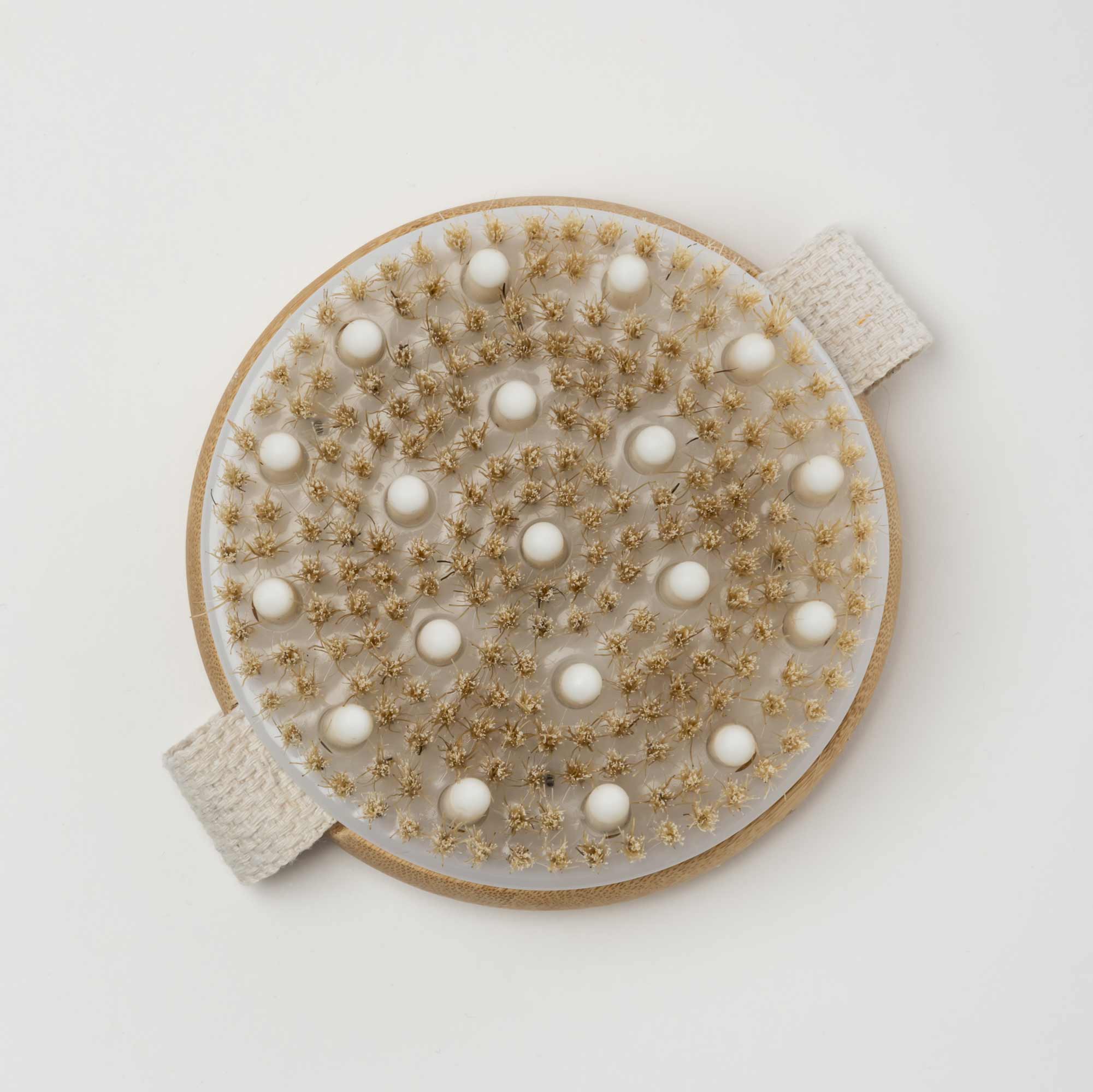 Round massage pad with textured surface on a white background. Victoria James Massaging Body Brush
