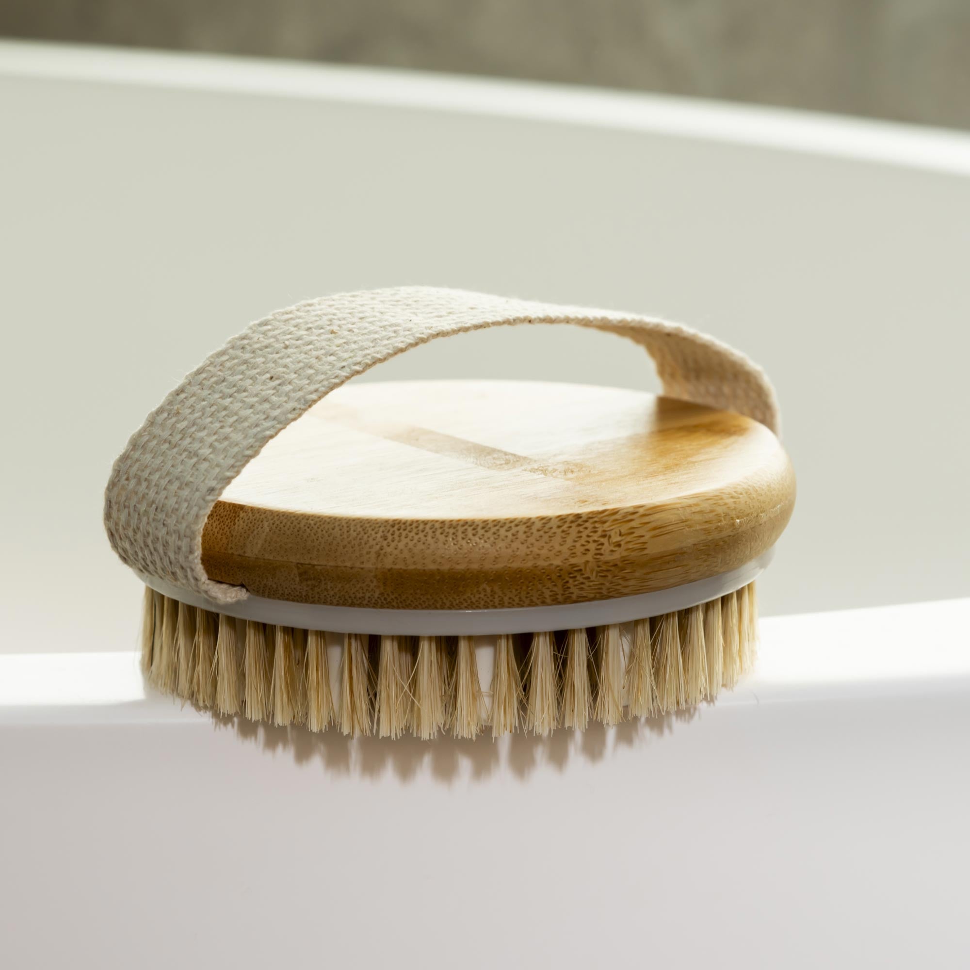 Body brush with wooden handle and bristles on a white surface. Victoria James Massaging Body Brush