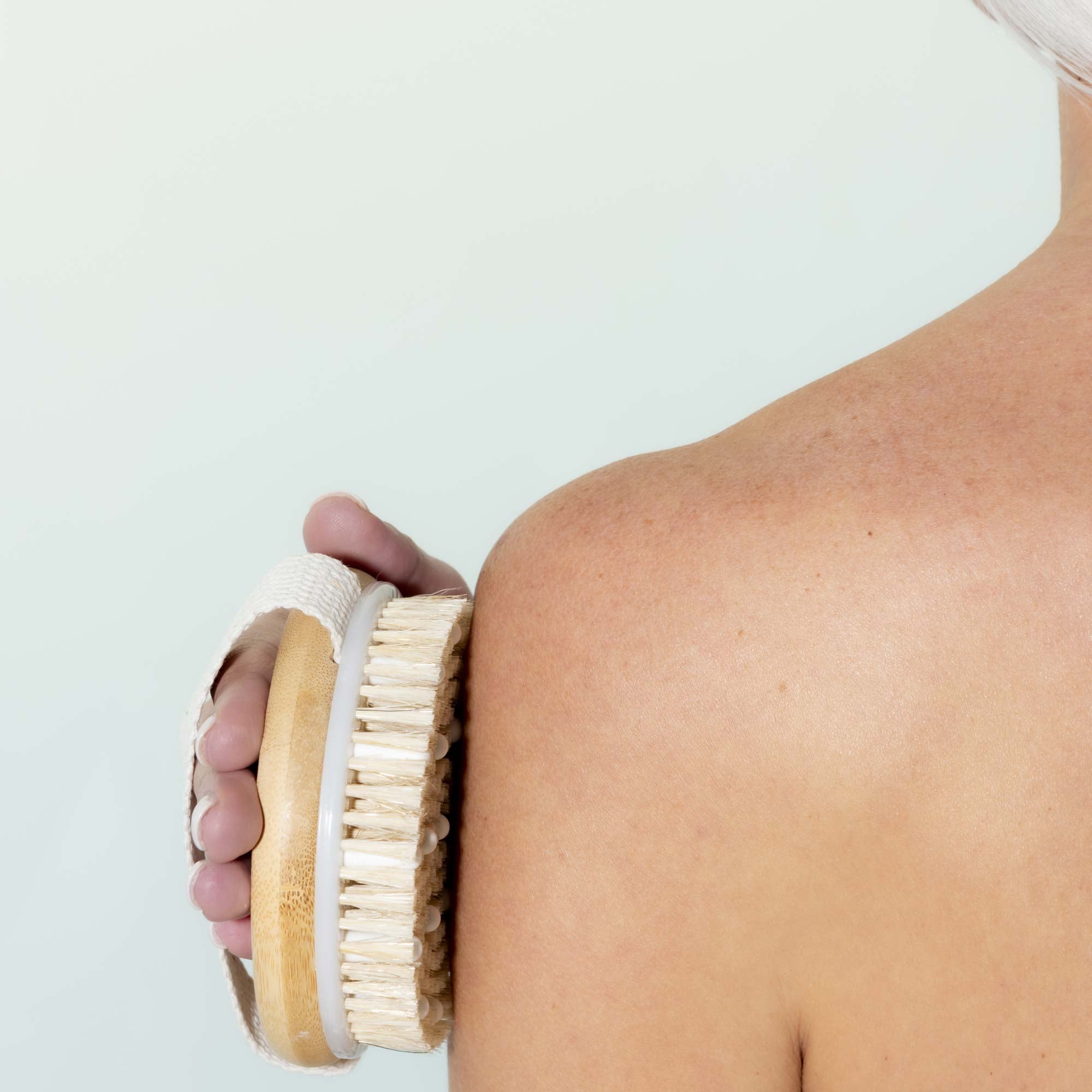 Person using a dry brush on their shoulder against a light background. Victoria James Massaging Body Brush