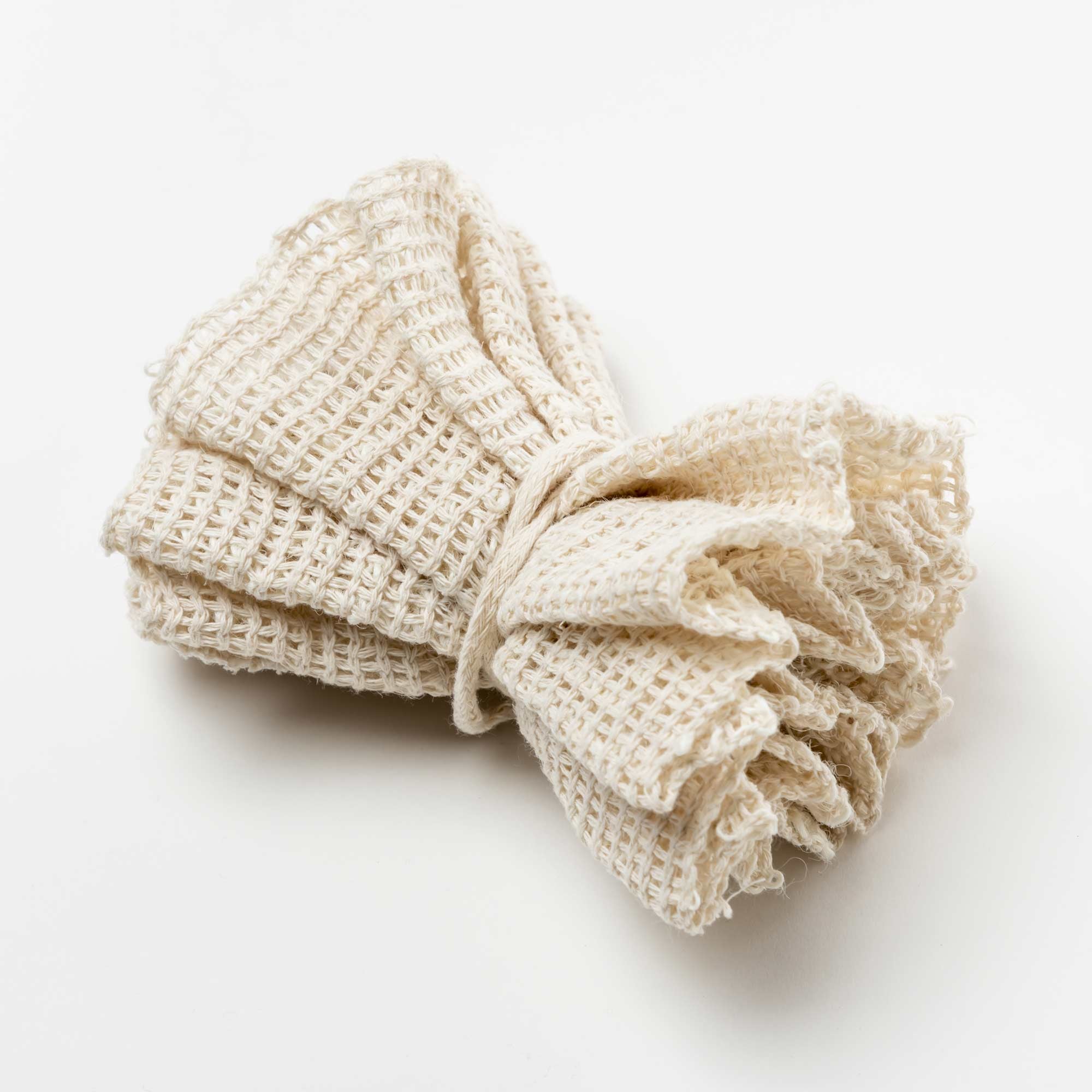 Folded beige towel on a white background. Victoria James Body Ramie Bath Puff