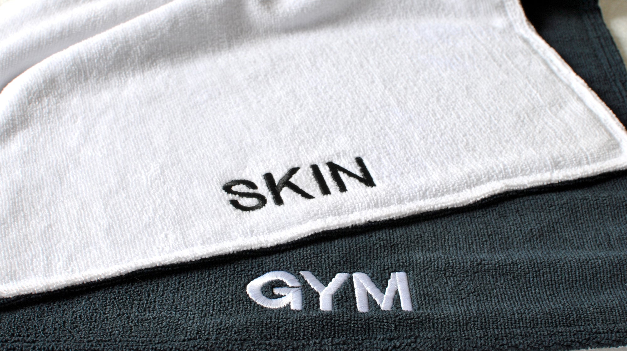 Text 'SKIN' on a white towel and 'GYM' on black fabric. Simply Clean Active Gym Buddy