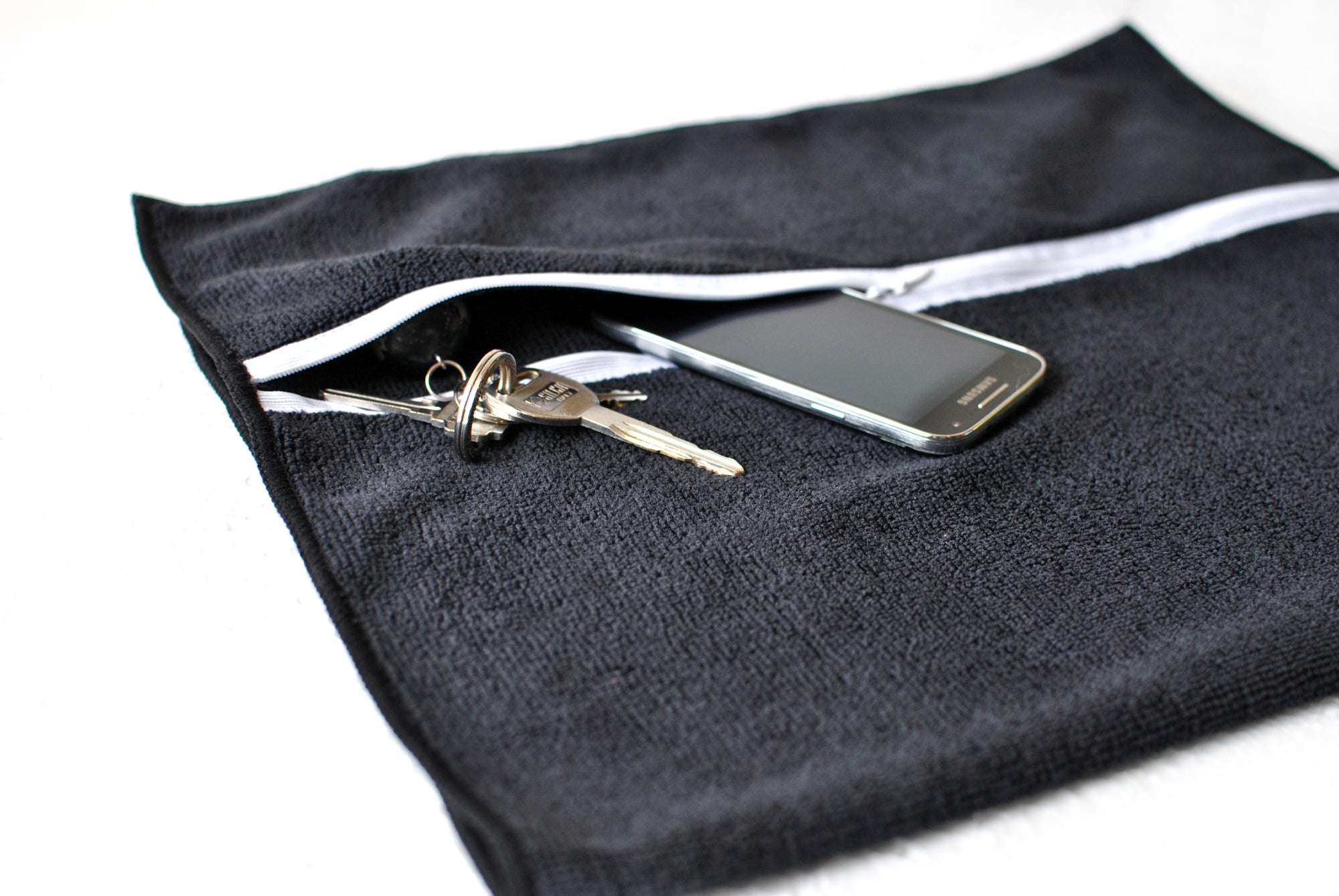 Black pouch with a white zipper containing keys and a smartphone on a light gray background. Simply Clean Active Smart Towel