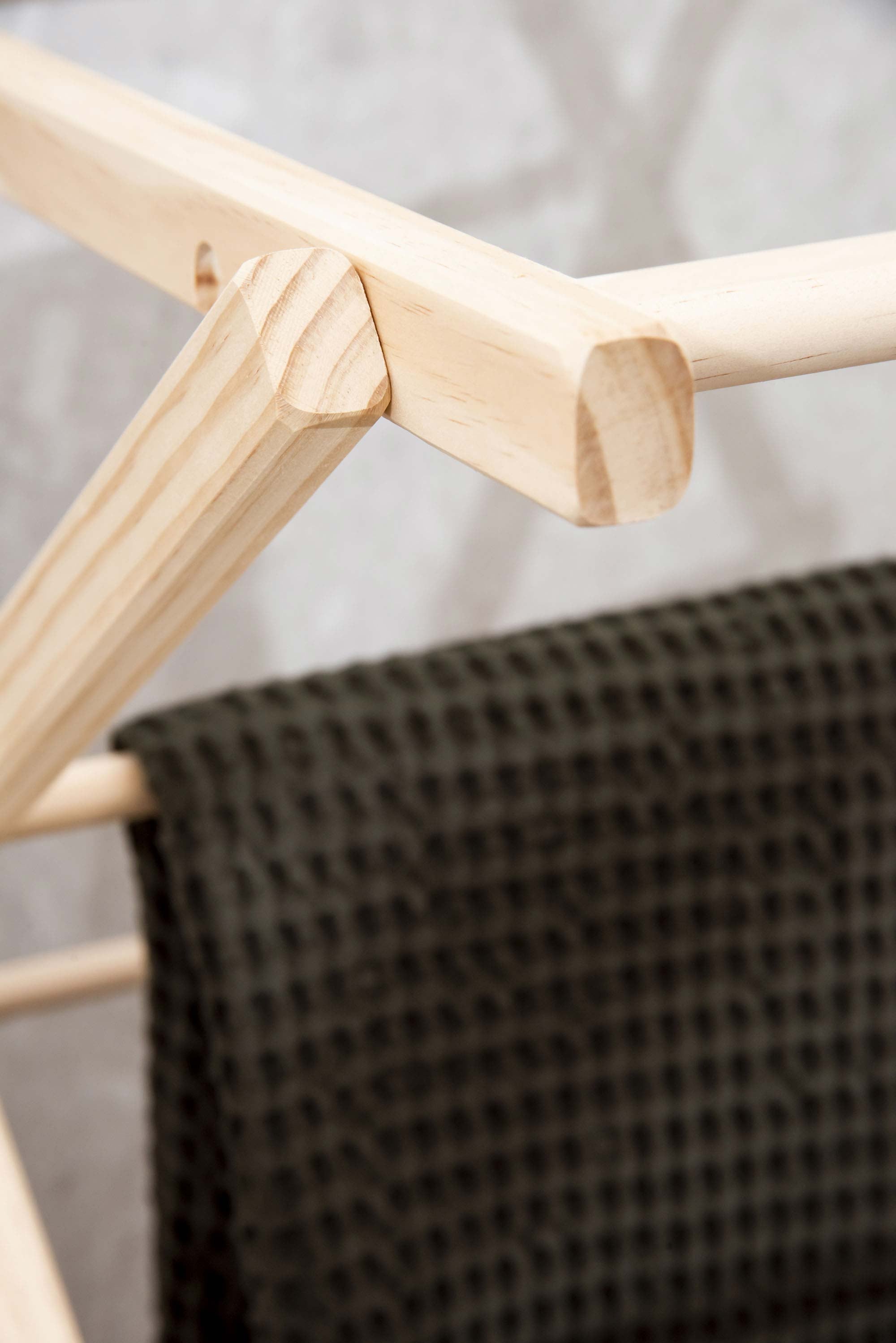 Wooden clothes airer with a black textured garment on a light gray background. Victoria James Home Eco Deluxe Clothes Airer