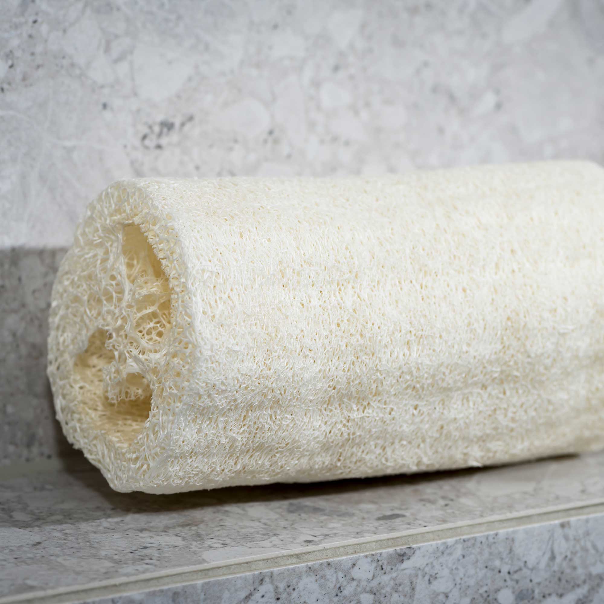 Roll of white paper towel on a marble surface with a gray marble background. Victoria James Body Loofah Brush
