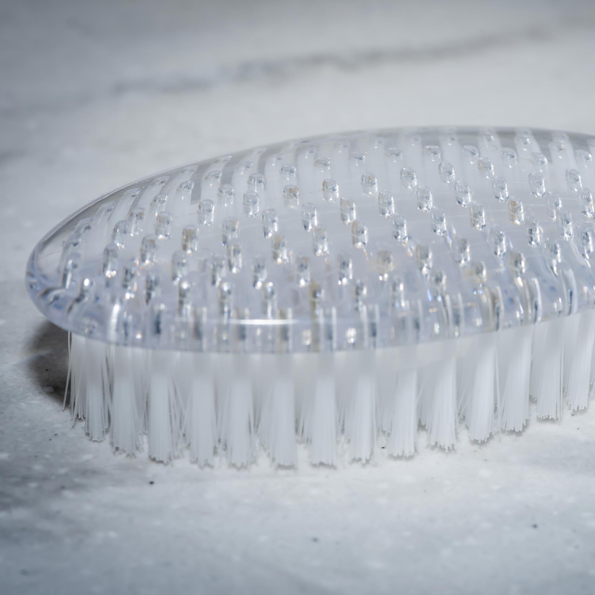 Clear nail brush with bristles on a light gray background. Victoria James Body Bath & Shower Brush