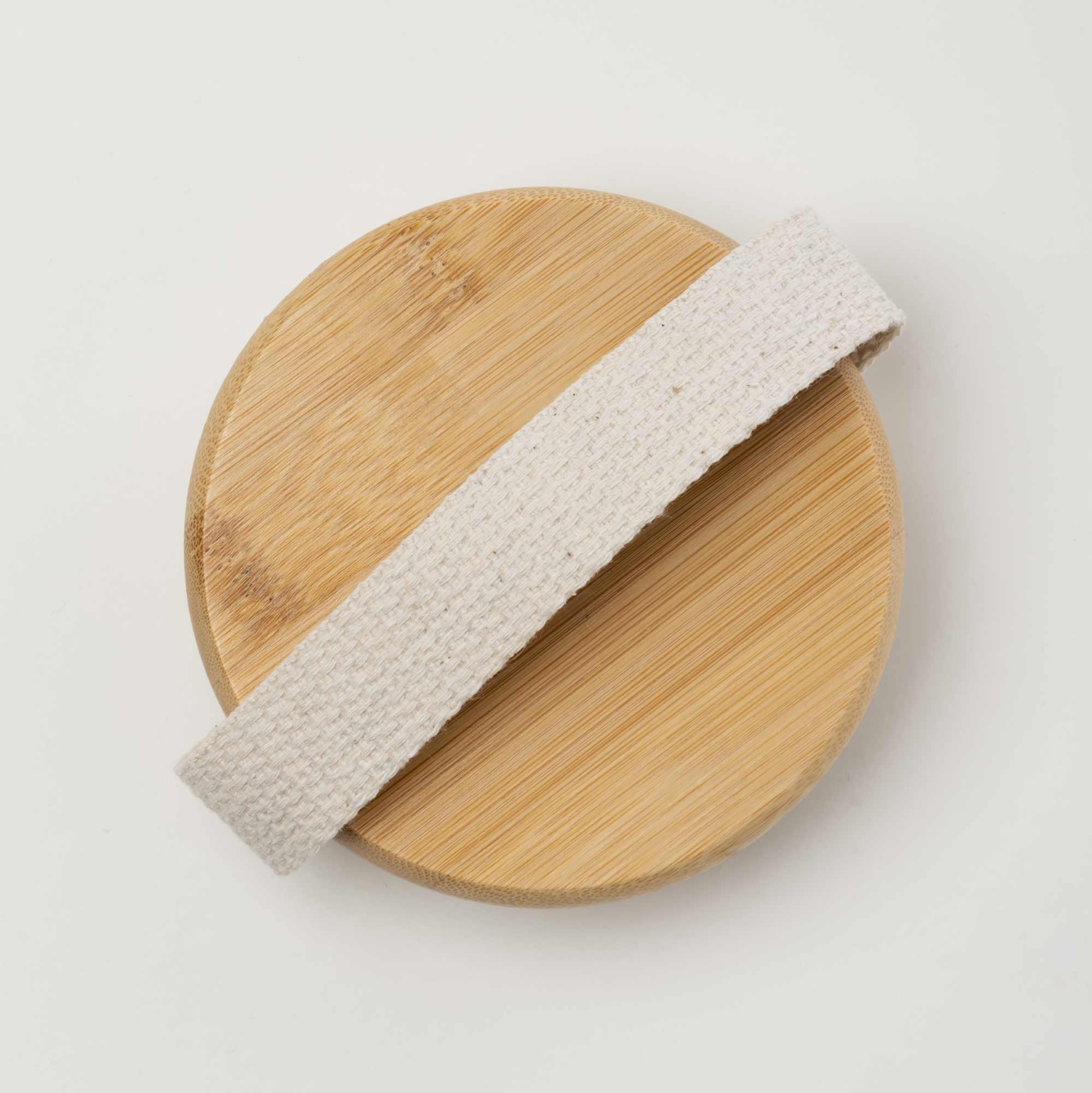 Wooden cutting board with a beige woven handle on a light gray background. Victoria James Massaging Body Brush