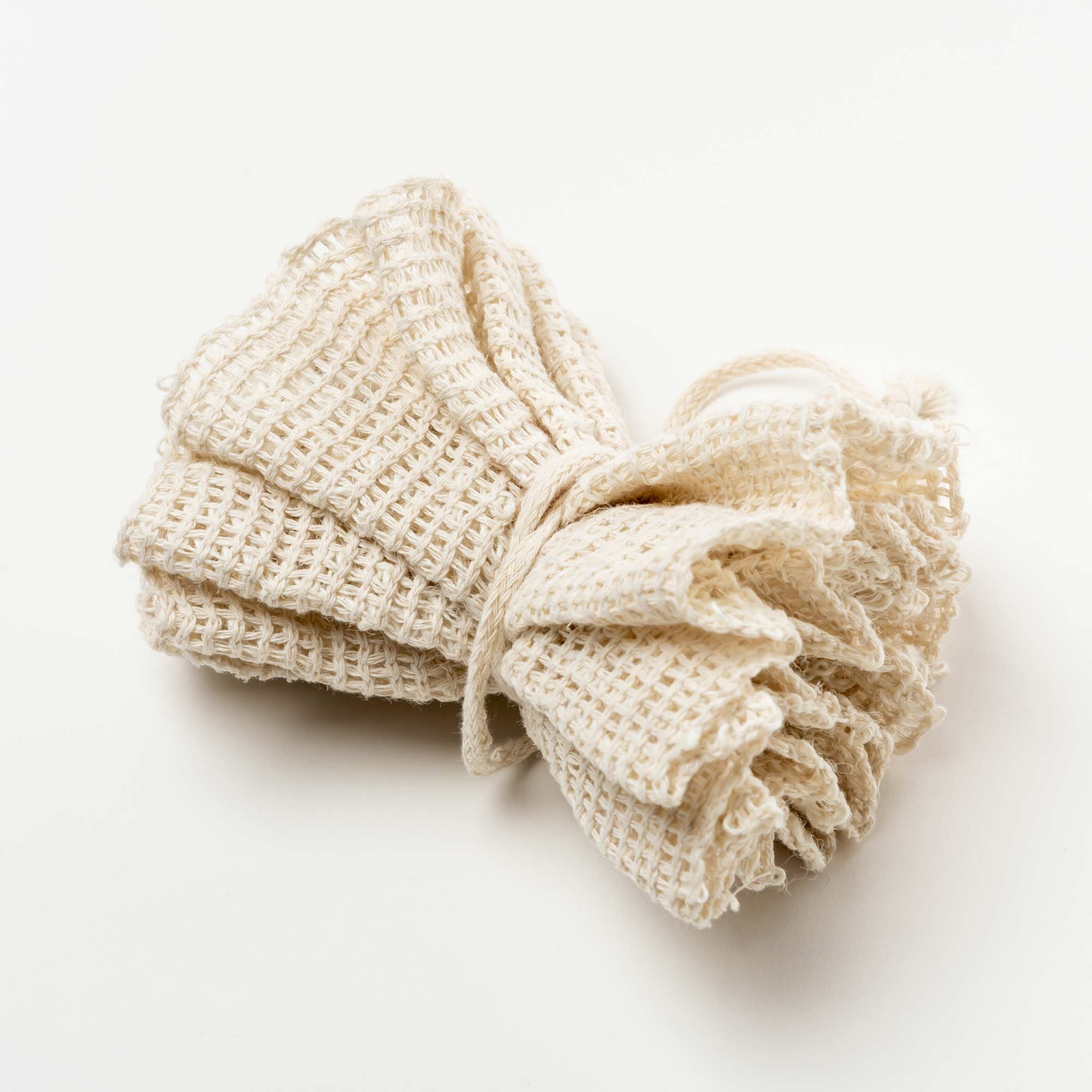 Folded beige towel on a white background. Victoria James Body Ramie Bath Puff
