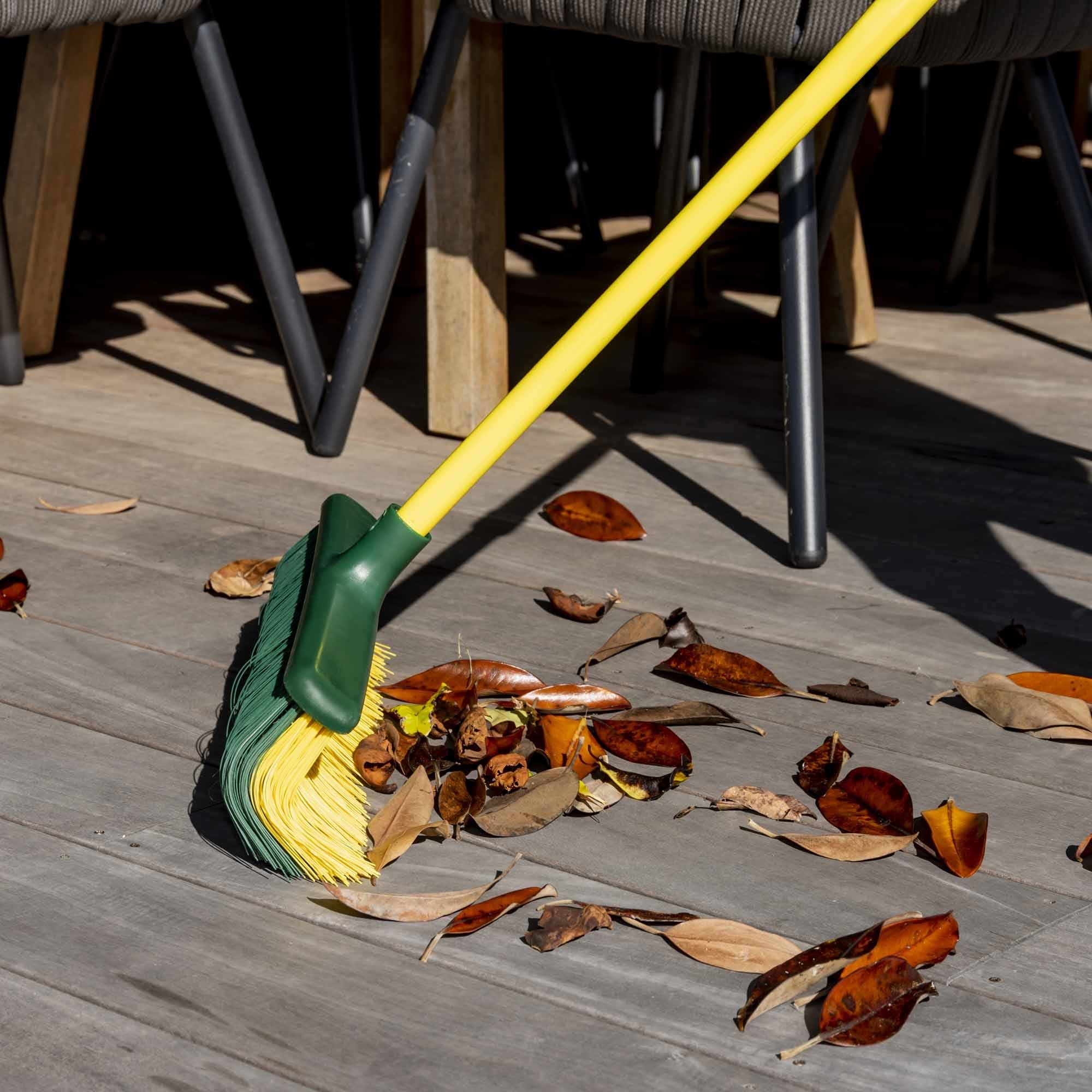 Mop with yellow head and green handle cleaning leaves on a wooden deck. Simply Clean 2IN1 Broom & Rake